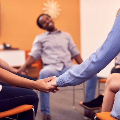 Multi-Cultural Group Of Men And Women Joining Hands At Mental Health Group Therapy Meeting Multi-Cultural Group Of Men And Women Joining Hands At Mental Health Group Therapy Meeting
